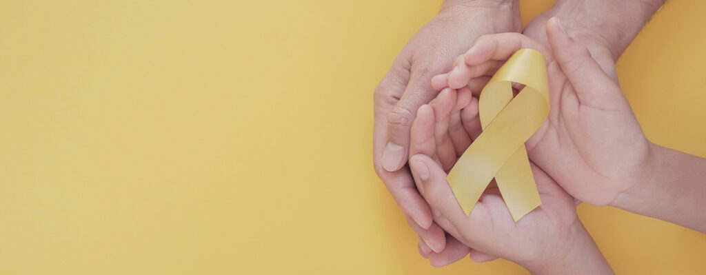 manos sosteniendo moño amarillo, representación de leucemia infantil