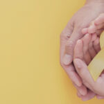 manos sosteniendo moño amarillo, representación de leucemia infantil