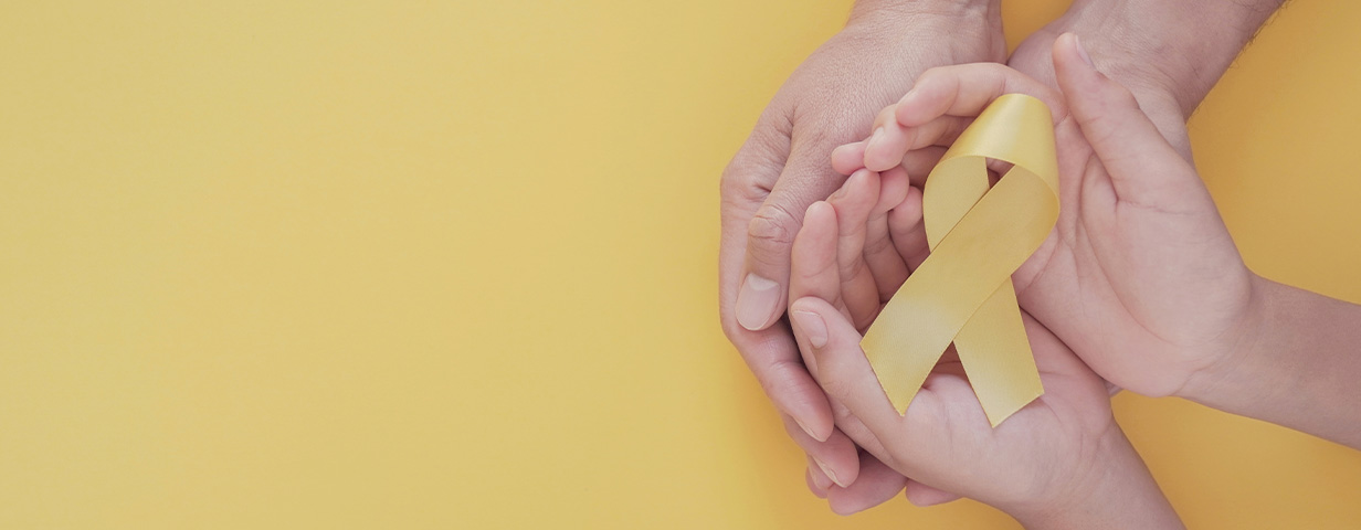 manos sosteniendo moño amarillo, representación de leucemia infantil