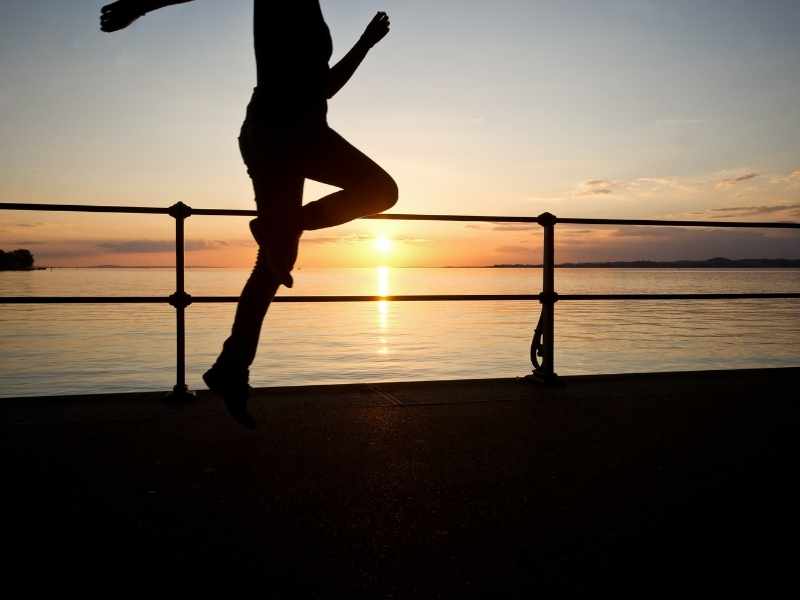 Silueta de una persona corriendo al aire libre frente al mar durante el amanecer, representando el hábito del ejercicio regular para una vida activa.