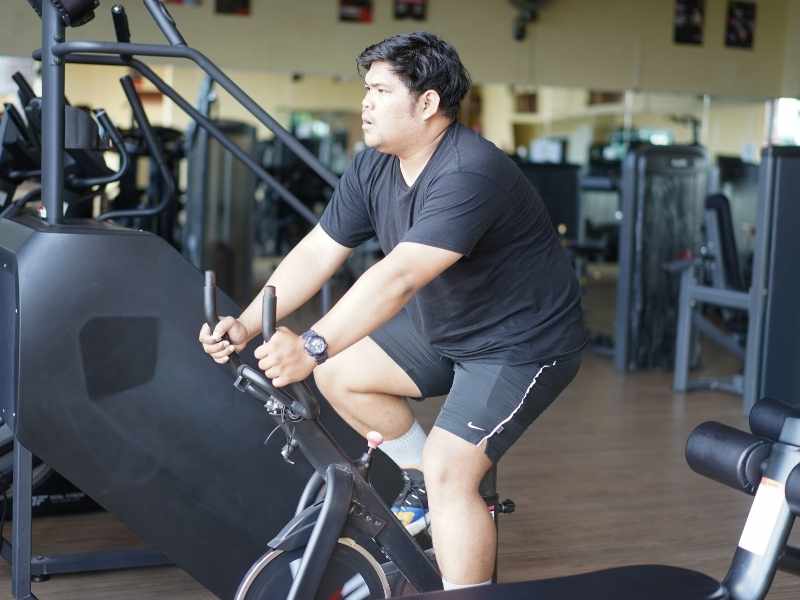 Hombre joven ejercitándose en una bicicleta fija dentro de un gimnasio, mostrando un momento de esfuerzo personal enfocado en mejorar la condición física.